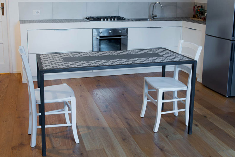 Tavolo con telaio in ferro scuro e piano in cementine decorate in una cucina con parquet